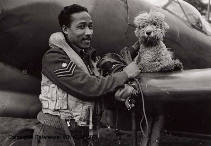 Flight Sergeant James Hyde of San Juan, Trinidad, a Spitfire pilot who arrived in Britain in 1942 to begin his training,
Pictured here in 1944 with the Squadron’s mascot, a dog called ‘Dingo’ (IWM) Reference CH11978
