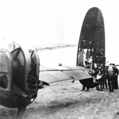 This view of Lancaster DV305 from the port side shows some of the severe damage inflicted, and deflated tail wheel, with right, surviving crew members discussing their ordeal.